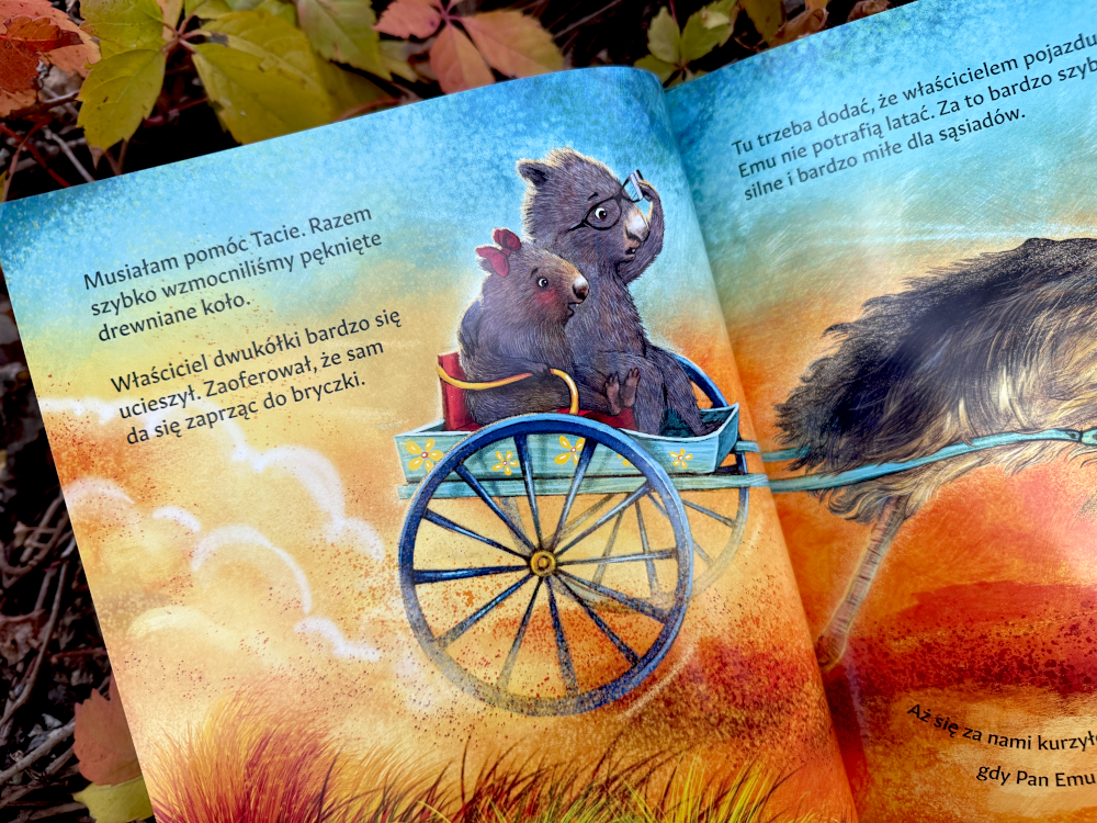 Ilustracja przedstawia Malinkę Wombat i jej tatę w bryczce zaprzęgniętej do emu, jadących do portu po kapibarę Tarararę – scena z książki dla dzieci Malinka Wombat i Kapibara.