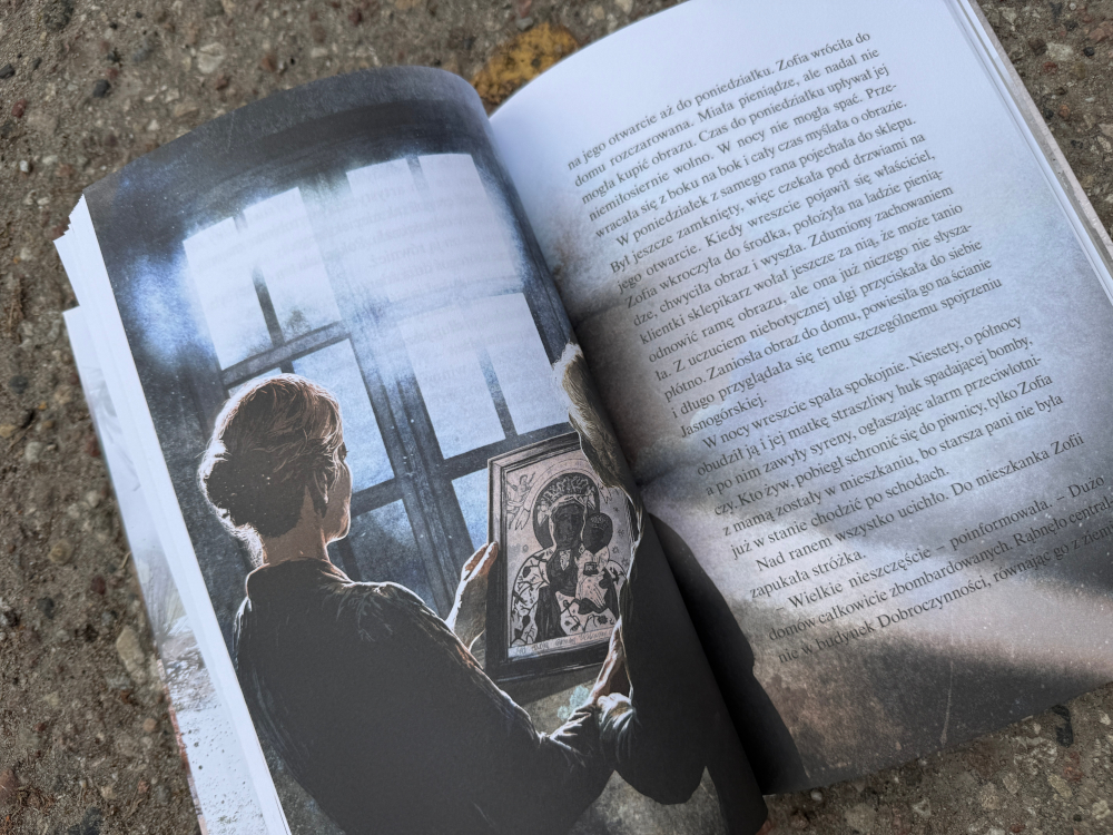 Książka Konspiratorka sfotografowana w ciepłej aranżacji z widokiem na okno– idealna lektura na jesienny wieczór.