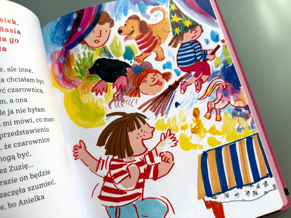 Basia i dzieci stojące na scenie podczas przedszkolnego przedstawienia; rodzice siedzą na widowni, oklaskując młodych aktorów.