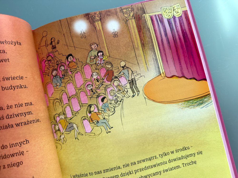 Basia siedząca w teatralnym fotelu, wpatrzona w scenę, na której występuje krecik; w tle widać miękkie światło sceniczne i elementy dekoracji.