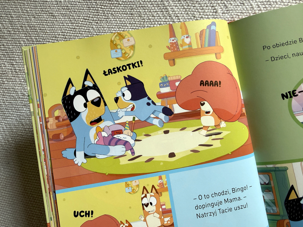 ata Bluey udaje maszynę-lapacza, trzymając ręce jak chwytak. Bluey i Bingo patrzą na niego z rozbawieniem, szykując się do zabawy. Ilustracja pełna ruchu i humoru.