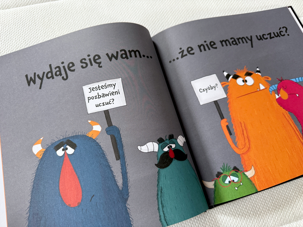 Rozkładówka książki o emocjach dla dzieci – kolorowe potwory z transparentami o uczuciach.