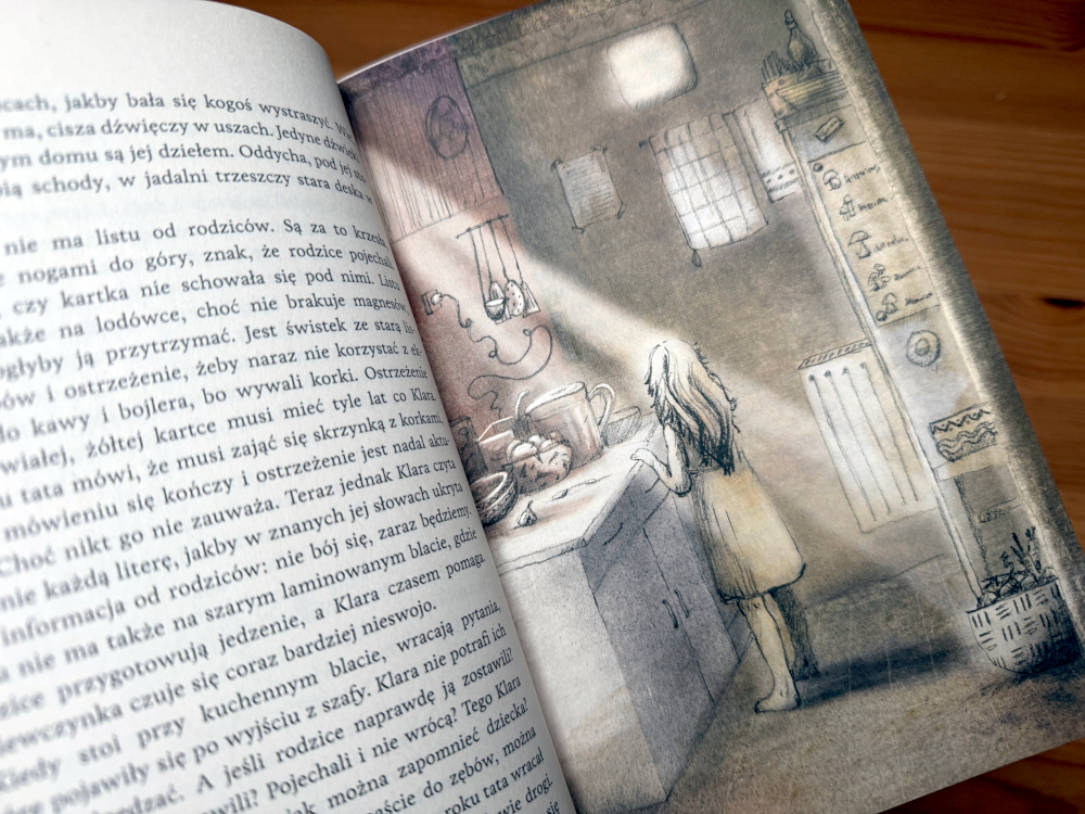 lustracja z książki „Wylinka” – Klara stoi przy stole w drewnianej kuchni, w której światło wpada przez okno, podkreślając atmosferę samotności i niepokoju.