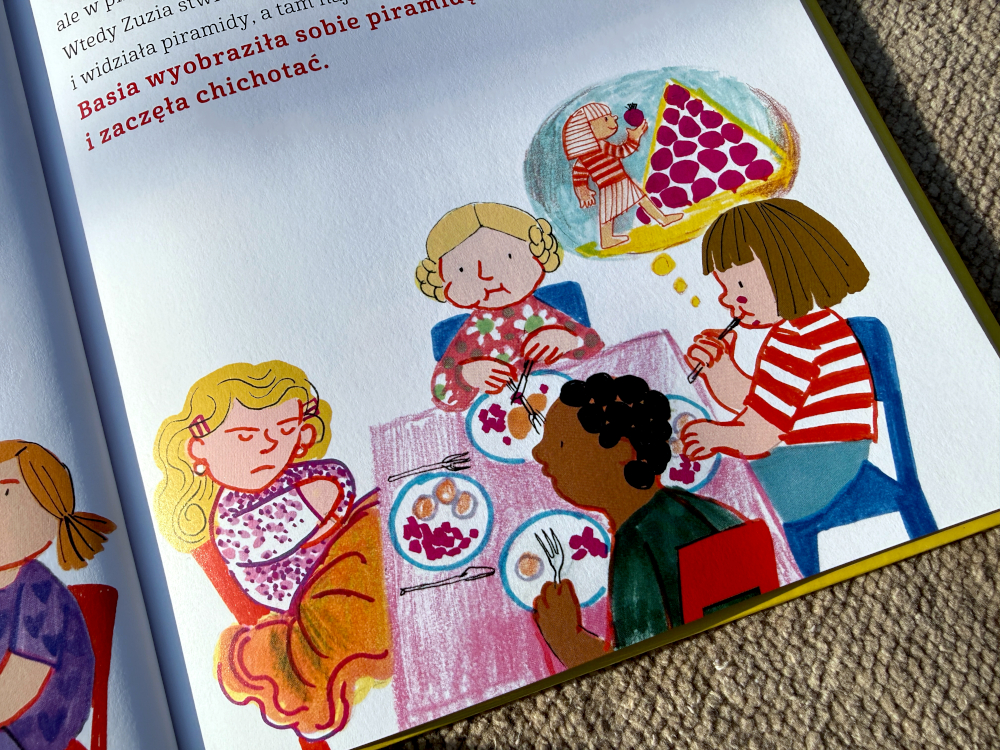 Ilustracja z książki Basia i jedzenie – dzieci siedzą przy stole i jedzą posiłek, scena z przedszkola, różnorodne dania