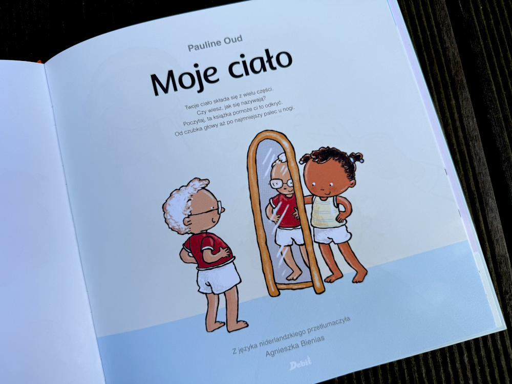 Otwarte rozkładówki książki Moje ciało z ilustracjami dzieci oraz lustrem pokazującymi dzieciom jak wyglądają