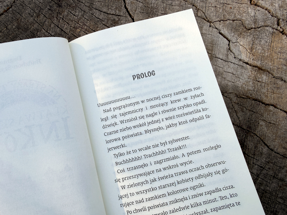 Otwarte strony książki Na straży tajemnic Klątwa skarbu Inków z widocznym prologiem na tle drewnianej powierzchni