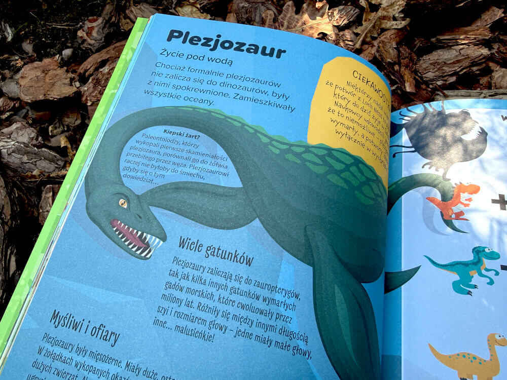Otwarte strony książki Spacer wśród dinozaurów prezentujące różne gatunki dinozaurów i aktywności dla dzieci