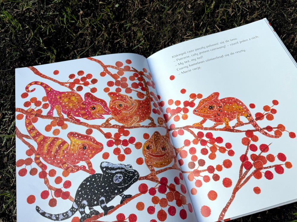 Otwarta książka „Czarny Kameleon” Sun-sun Lee z ilustracją kolorowych kameleonów siedzących na gałęziach z czerwonymi owocami.
