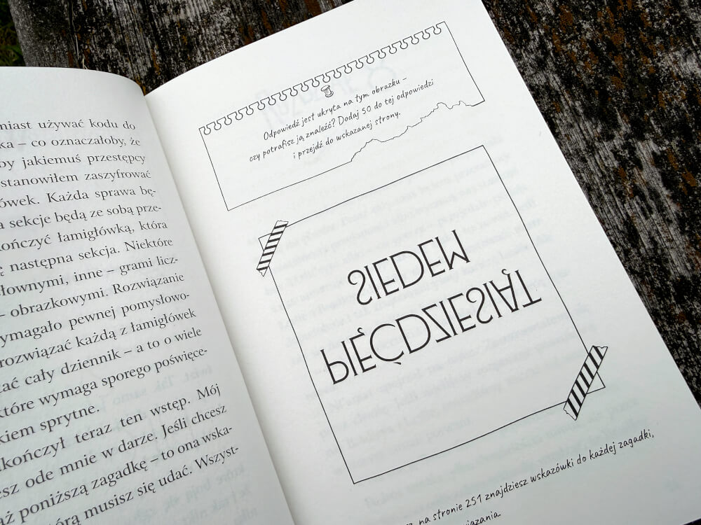 Fragment otwartej książki, na której prawej stronie znajduje się zagadka z napisem ZIEDEW w lustrzanym odbiciu oraz instrukcja dodania 50. Obok zagadki narysowane są paski przypominające gumki recepturki.