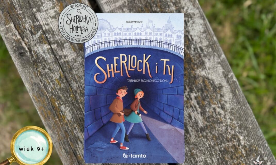 ￼Niebieska okładka książki Sherlock i Ty. Tajemnica zaginionego domu z ilustracją dwójki dzieci w tunelu na tle Londynu, leżąca na drewnianej ławce. W rogu znaczek wiek 9+
