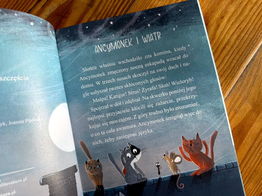 Otwarta książka Ancymonek na tropie szczęścia z tytułem rozdziału Ancymonek i wiatr oraz ilustralcją kotów.